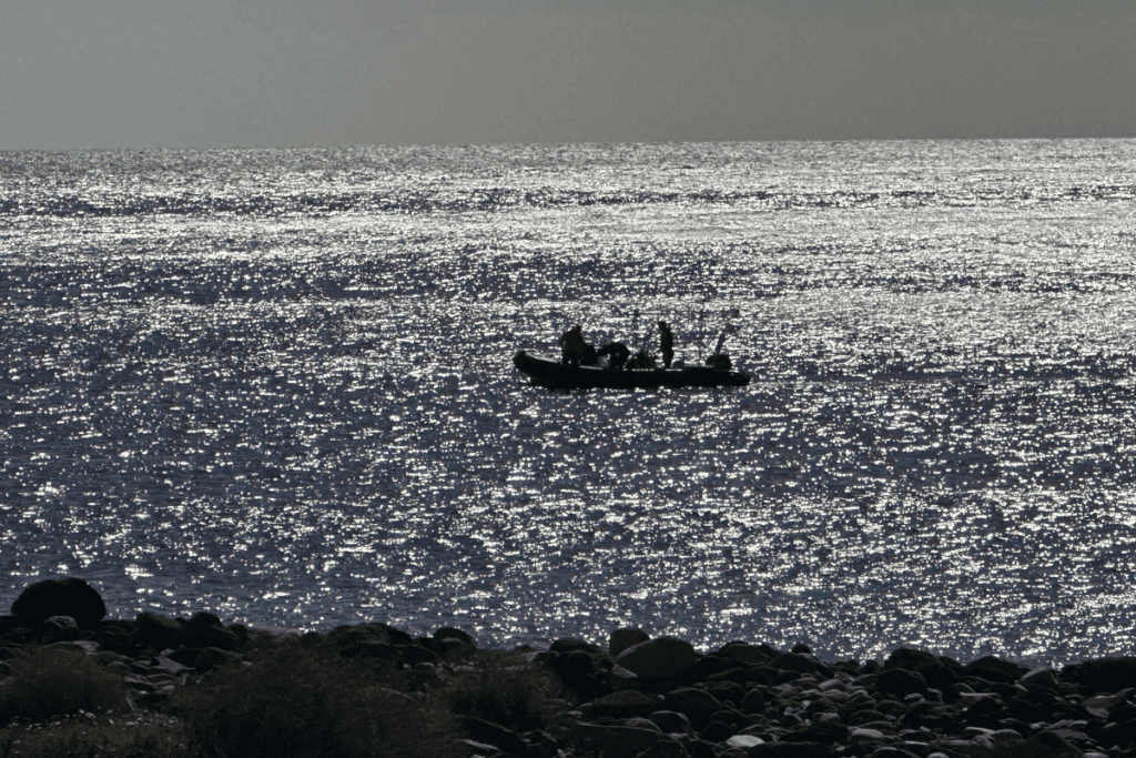 Ein Boot kehrt von Playa Del Cabrito La Gomera, auch bekannt als Cabrito Beach, Kanarische Inseln, Spanien, mit Kiesstrand im Vordergrund nach San Sebastian zurück