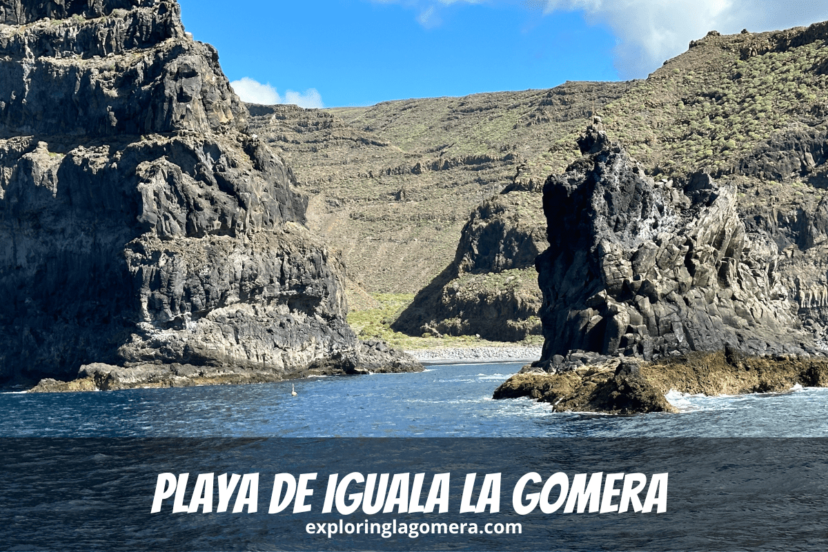 Mare blu e formazioni rocciose di fronte a Playa De Iguala La Gomera Isole Canarie Spagna con ripide montagne sullo sfondo