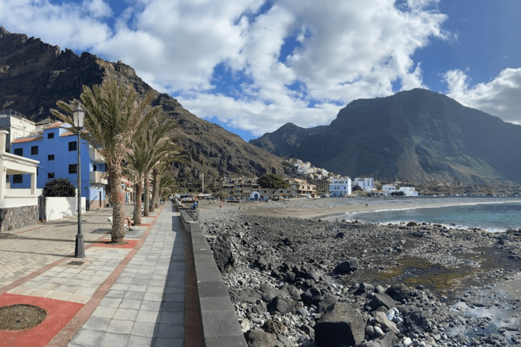 A Beach Of Sand And Pebble Called Playa De La Calera La Gomera Canary Islands Spain With A Promenade And Restaurants And Volcanic Mountains In The Background