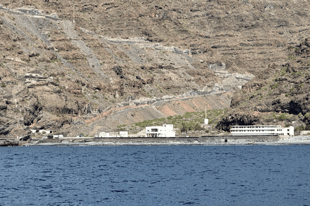 Verlassene Gebäude am Playa De La Rajita La Gomera Kanarische Inseln Spanien mit blauem Meer im Vordergrund und einer Straße auf einem steilen Berg im Hintergrund