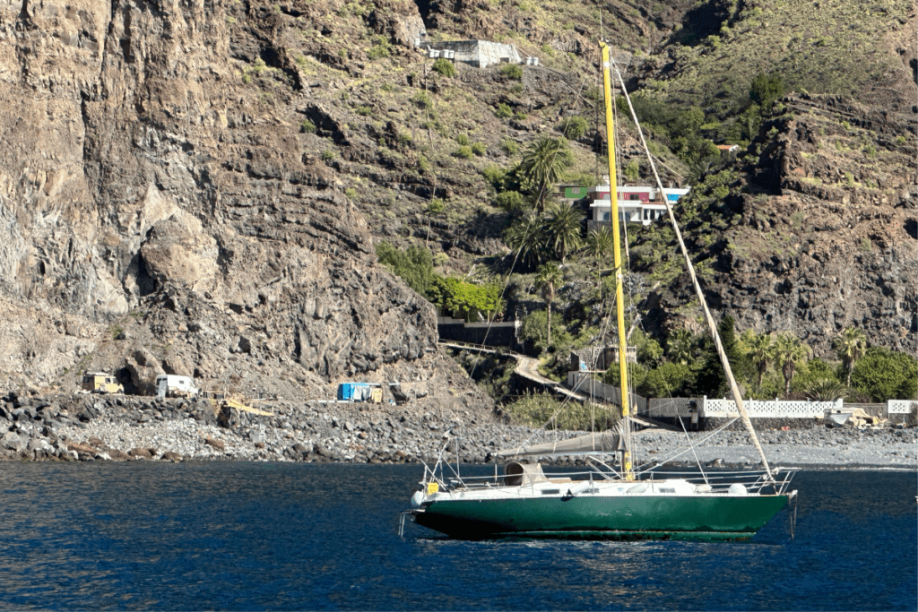 Un velero verde en el mar azul navega más allá de Playa de Las Arenas La Gomera Islas Canarias España con montañas en el fondo Una de las mejores playas de La Gomera 