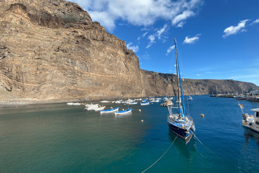 Barche nel porto con spettacolari scogliere vulcaniche in background in una giornata di sole a Playa De Vueltas La Gomera a Valle Gran Rey Isole Canarie Spagna