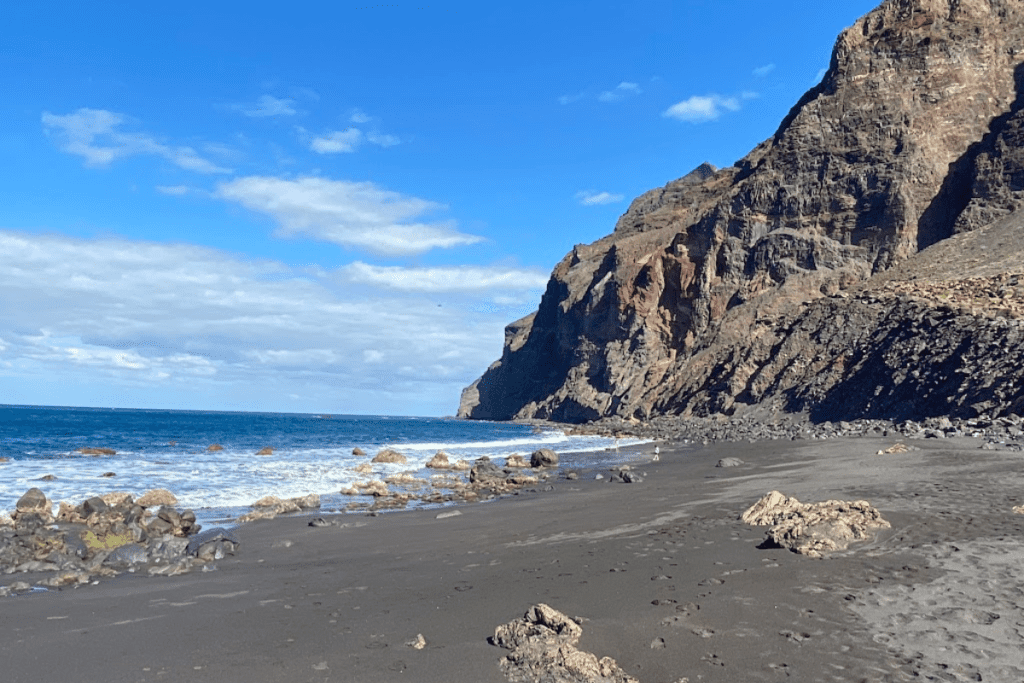 Sandstrand mit Wellen vom Meer und dramatischen Vulkangesteinen im Hintergrund an der Playa Del Inglés auf La Gomera im Valle Gran Rey auf den Kanarischen Inseln in Spanien