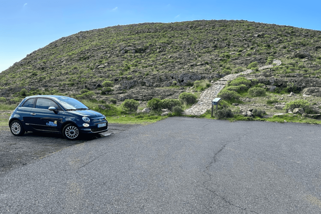 Petite voiture bleue dans le parking pour la randonnée à l'Ermita de San Isidro La Gomera Îles Canaries Espagne avec chemin pavé qui monte la colline en arrière-plan