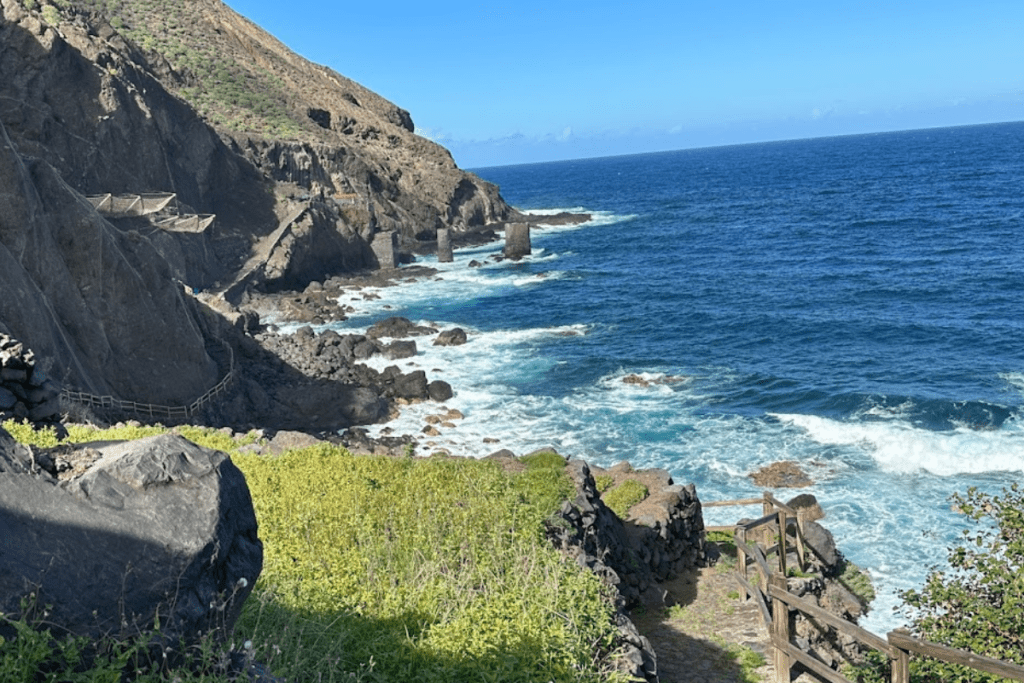 Der Weg im Vordergrund führt nach Pescante De Agulo, La Gomera, Kanarische Inseln, Spanien, mit blauem Meer und tosenden Wellen dahinter