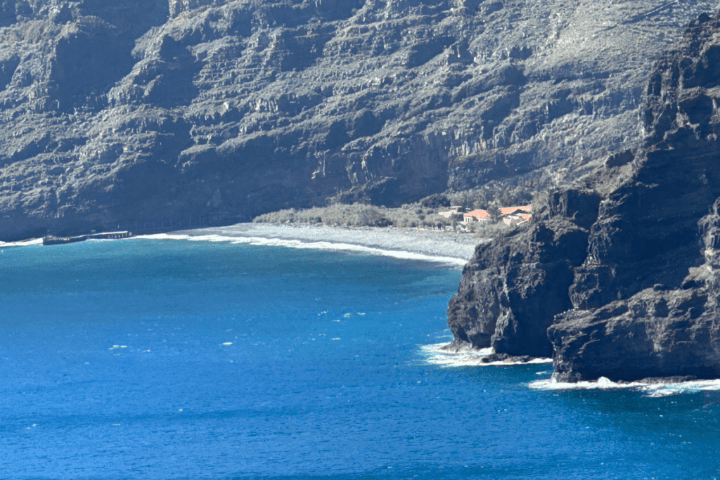 Blick auf Playa Del Cabrito von der Klippe mit Kiesstrand, schwarzen Klippen und glitzerndem Meer an einem sonnigen Tag. Einer der besten Strände in San Sebastian De La Gomera, Kanarische Inseln, Spanien